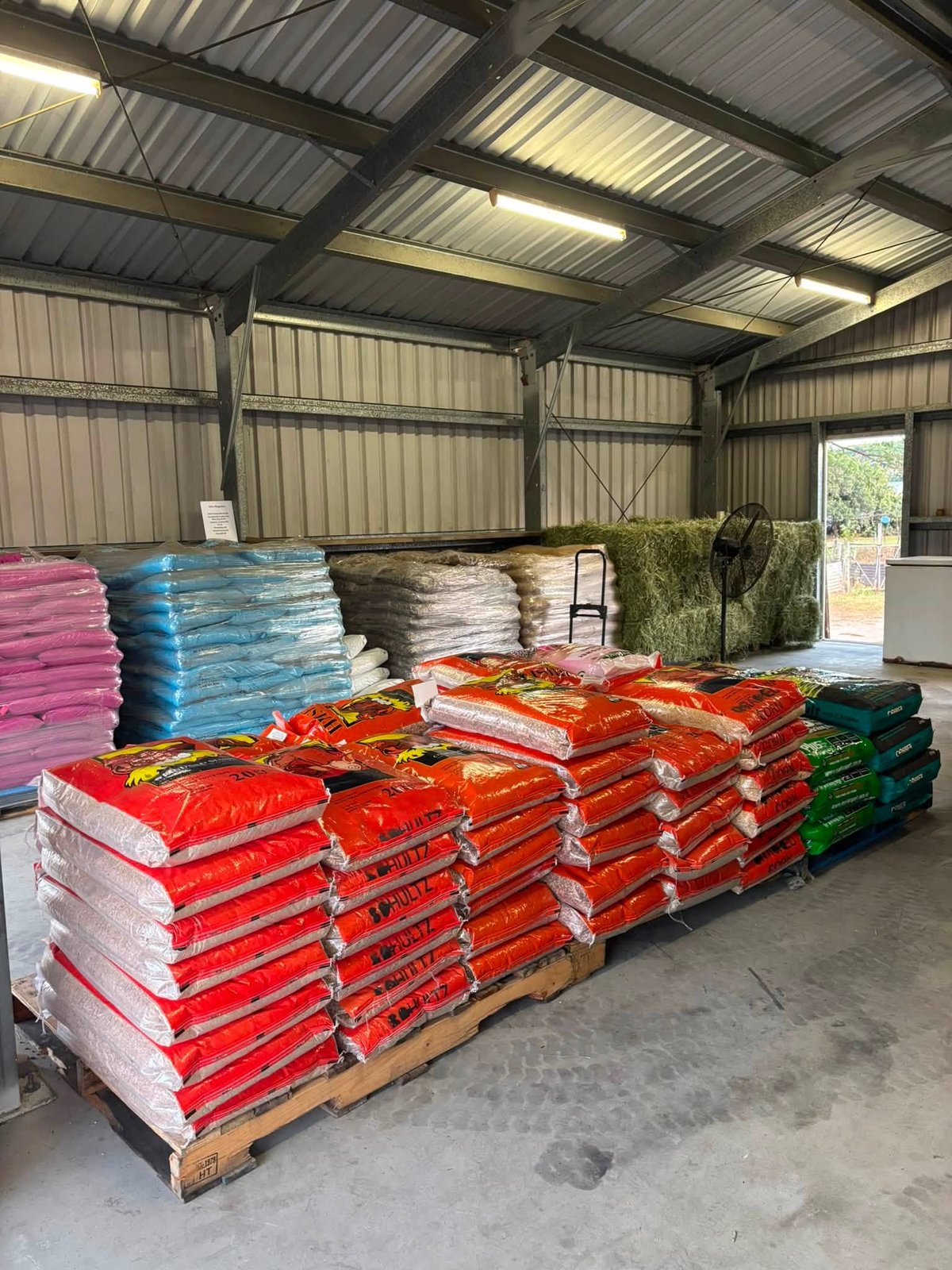Inside Giru Feed & Farm Supplies showing stacked feed bags, hay bales and farm supplies